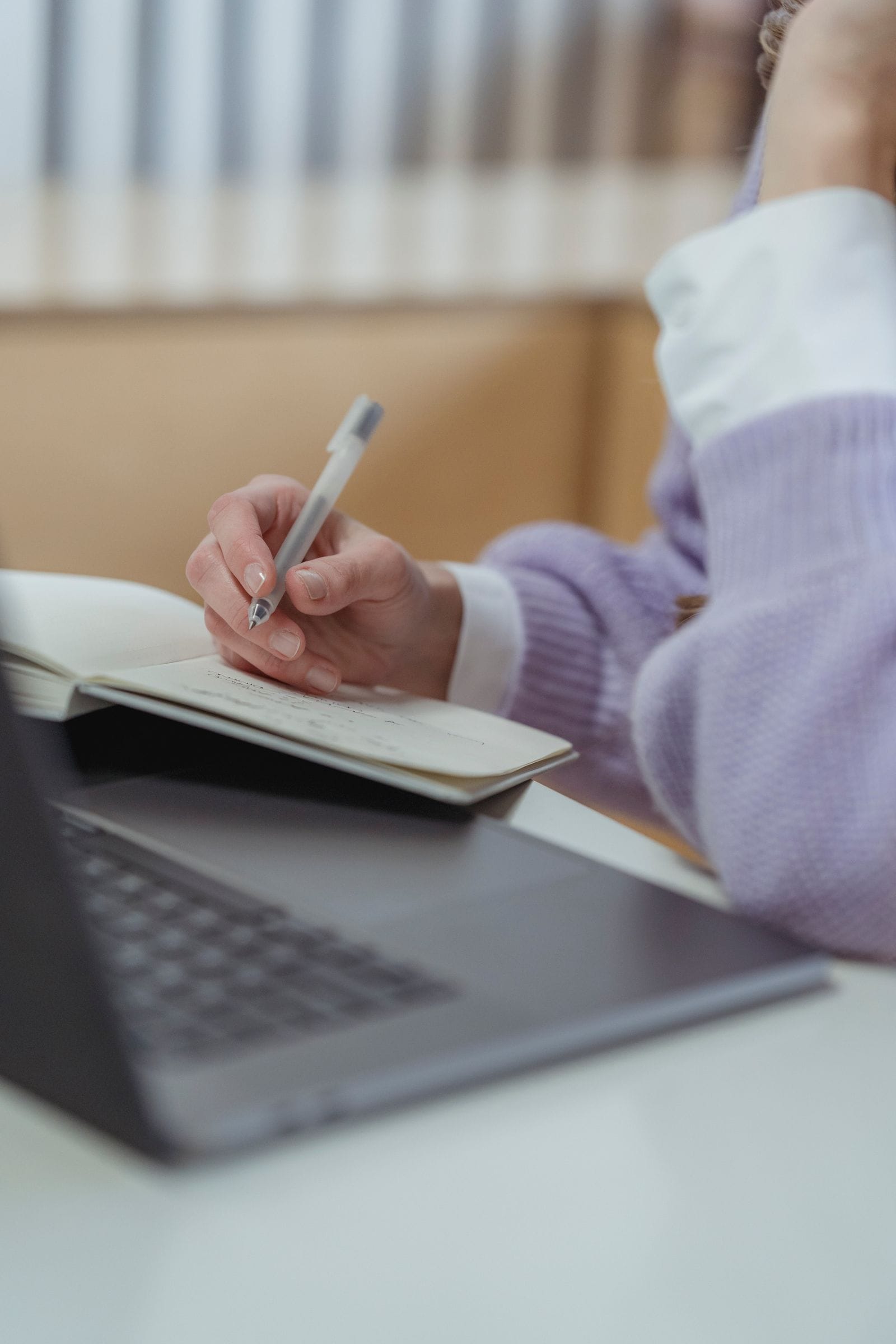 Manos tomando apuntes en un cuaderno junto a una laptop