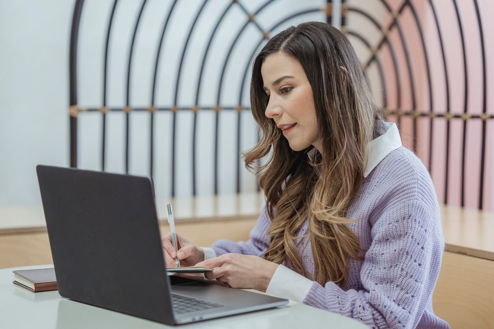 Mujer escribiendo en su cuaderno frente a una laptop