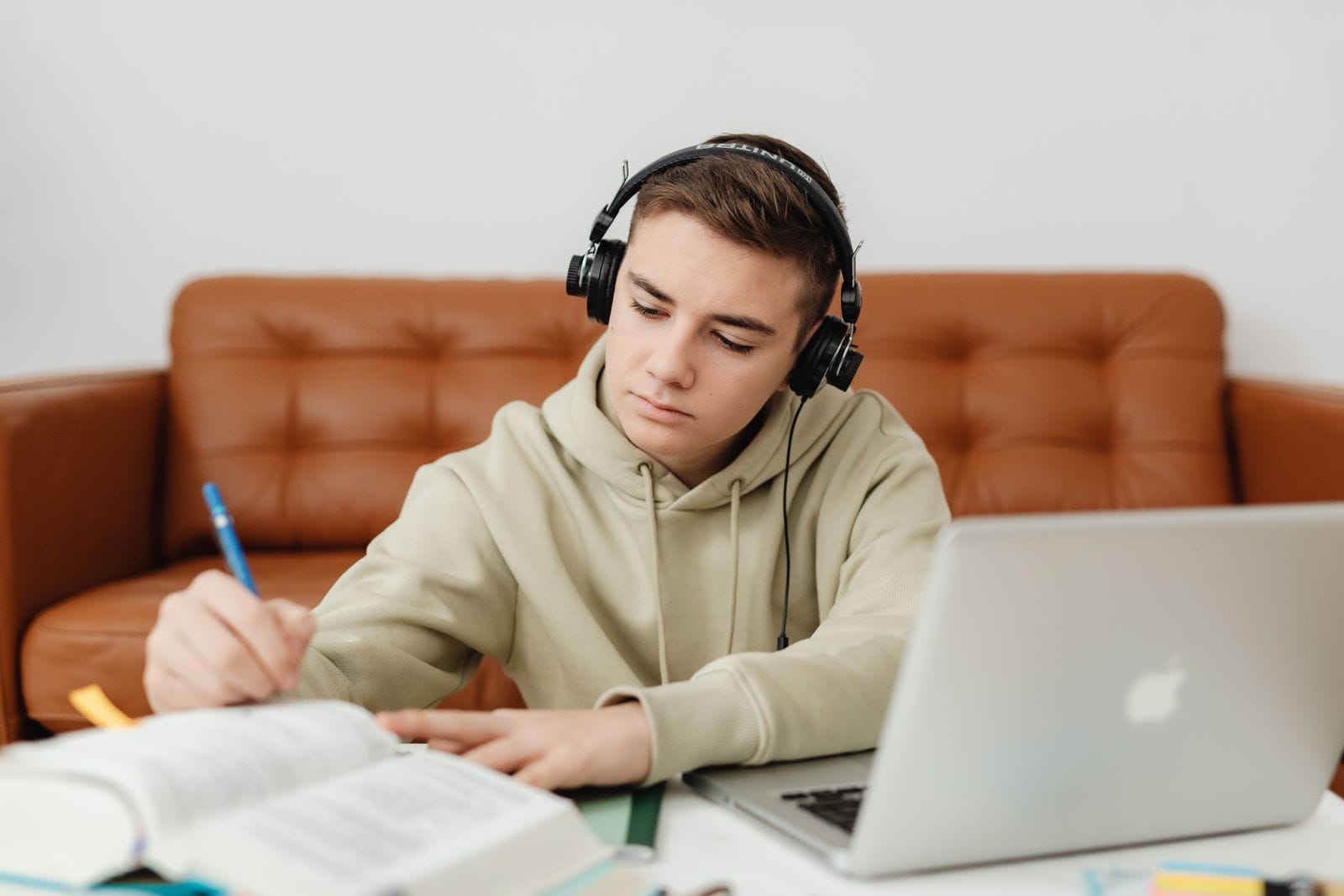 Joven con audífonos tomando apuntes junto a su laptop